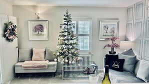 Una sala de estar con un árbol de Navidad, un sofá, una mesa baja con una botella de vino y cuadros en las paredes.