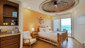 Un dormitorio con cama de madera, una silla, una mesita de noche, cafetera y vista al océano.