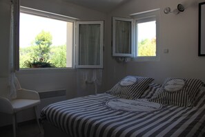 Un dormitori amb un llit, dues finestres, una cadira i un radiador.