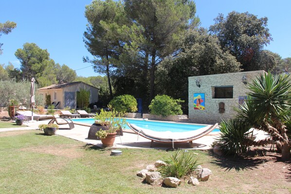 Zona de piscina amb gandules, un hamaca i un edifici petit amb un mural.