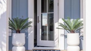 Una entrada de casa moderna con una puerta blanca, dos macetas y una terraza de madera.