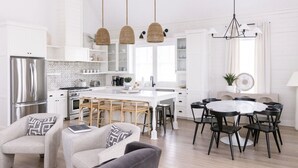 Una cocina moderna con armarios blancos, una isla central y un comedor con mesa y sillas redondas.
