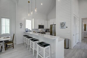 A modern kitchen with white cabinetry, a stainless steel refrigerator, and a bar area with stools. - Parkside Cottage@Cinnamon Shore near Town Center+Resort-Like Amenities (Port Aransas)