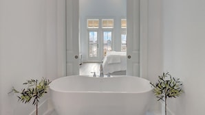 A bathroom with a freestanding bathtub, a mirror, and two potted plants.