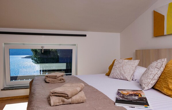 A modern hotel room with a large window offering a view of the sea, a neatly made bed with patterned pillows, and a book on the bed. - Awesome home in Medulin (Medulin)