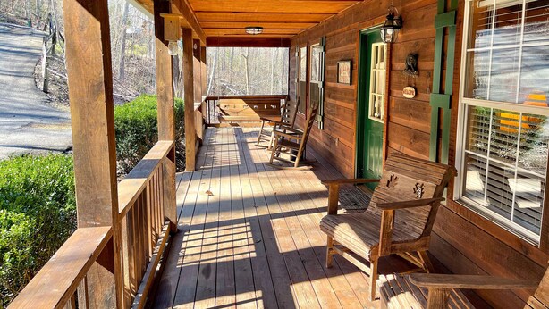 A wooden porch with a bench and a table, a green door, and a window with blinds.