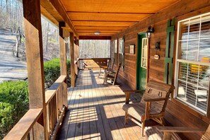 Une véranda en bois avec un banc et une table, une porte verte et une fenêtre avec des stores.