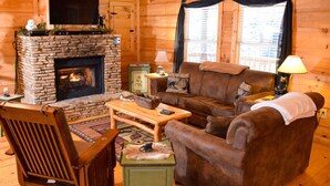 A cozy cabin interior with a stone fireplace, leather furniture, and a television mounted on the wall.