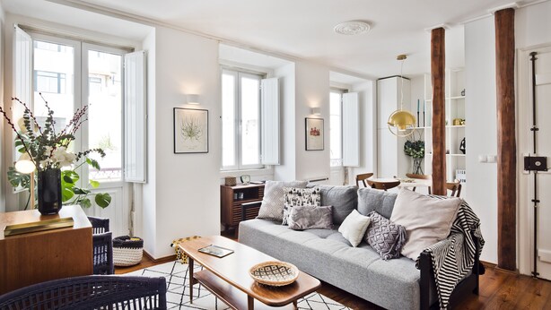 Uma sala de estar moderna com um sofá cinzento, mesa de centro de madeira e uma área de jantar com mesa e cadeiras de madeira.