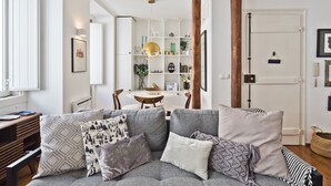 Uma sala de estar moderna com um sofá cinzento, almofadas estampadas, uma mesa de centro de madeira e uma estante branca.
