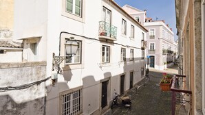 Uma rua de paralelepípedos estreita, ladeada por edifícios históricos com varandas, e uma scooter estacionada na lateral.