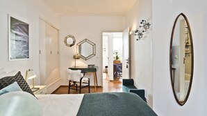Quarto com cama, escrivaninha, cadeira, espelho e porta que dá para um banheiro.