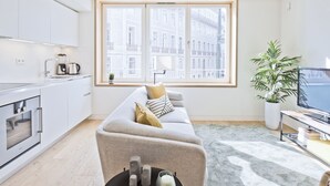 A modern living room with a sofa, a coffee table, a TV, and a large window with a city view.