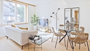 A modern living room with a sofa, TV, dining table, chairs, and a large window.