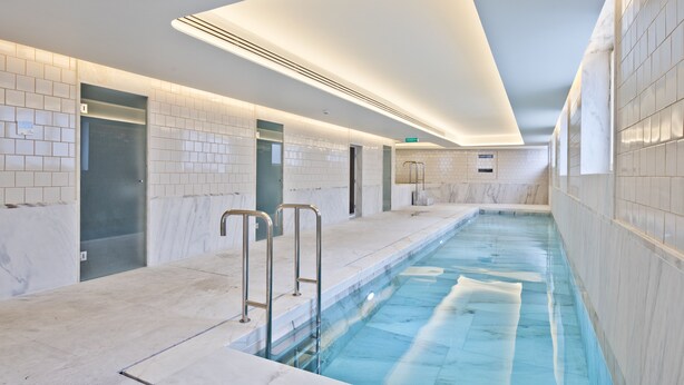 A modern indoor swimming pool with clear water, tiled walls, and a sleek design.