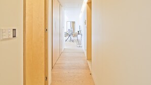 A hallway with wooden doors, a light-colored floor, and a dining area in the distance.