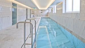 A modern indoor swimming pool with clear water, marble walls, and metal railings.