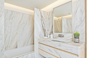 Une salle de bain avec des murs en marbre, un lavabo, un miroir et une plante en pot.