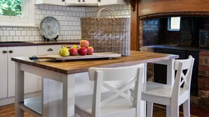 A kitchen with a wooden table, white chairs, a wicker basket, and a tray with apples. - Hillside - in central Daylesford, period home close to lake, shops and day spas (Daylesford)
