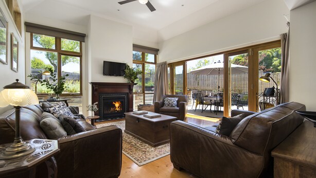 A spacious living room with leather sofas, a fireplace, and large windows offering views of the backyard. - Hillside - in central Daylesford, period home close to lake, shops and day spas (Daylesford)