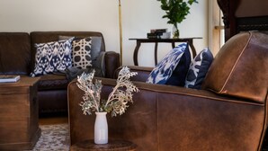 A brown leather sofa with patterned cushions, a white vase with dried flowers, and a small wooden side table. - Hillside - in central Daylesford, period home close to lake, shops and day spas (Daylesford)