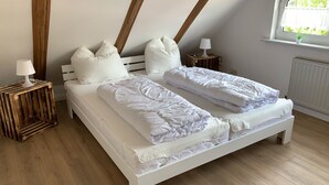 A bedroom with a wooden bed frame, white bedding, and a small bedside table with a lamp.