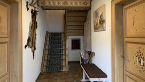 A hallway with a wooden staircase, a bench, and a door with a coat of arms.
