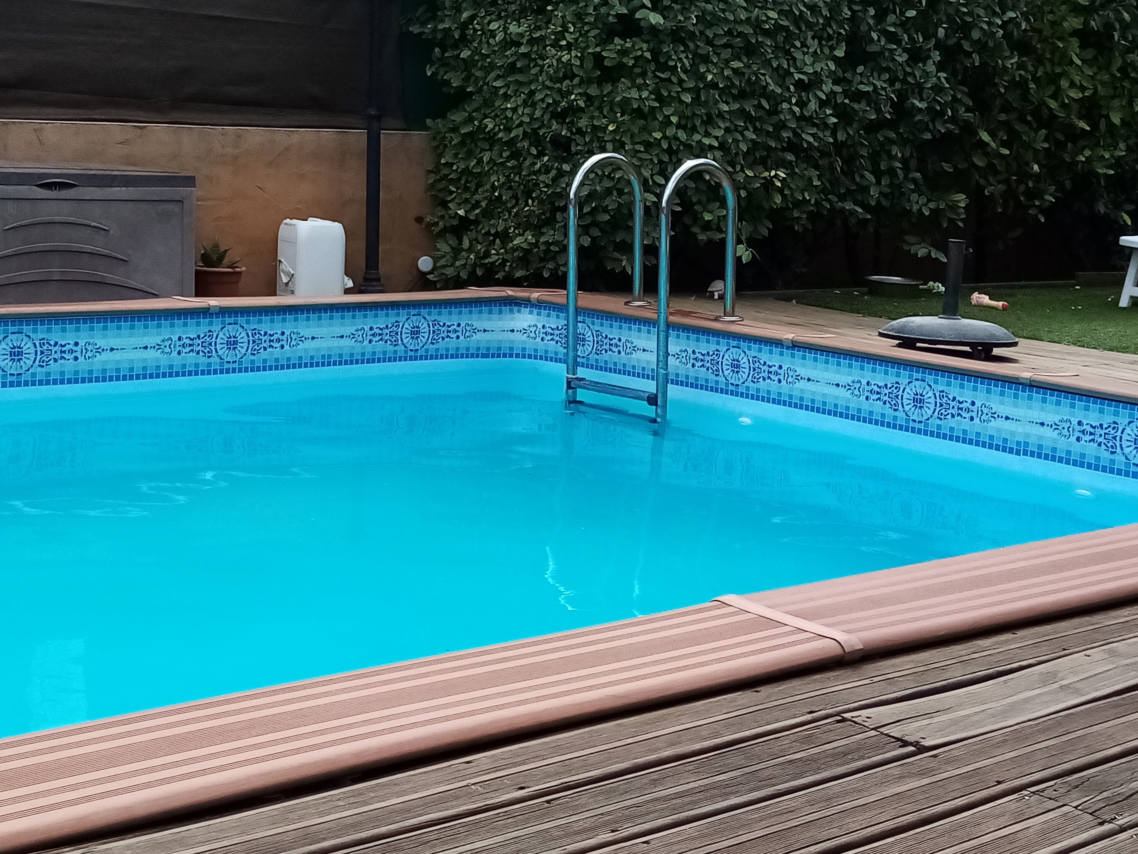 Una piscina rectangular con borde de azulejos azules y una cubierta de madera alrededor.