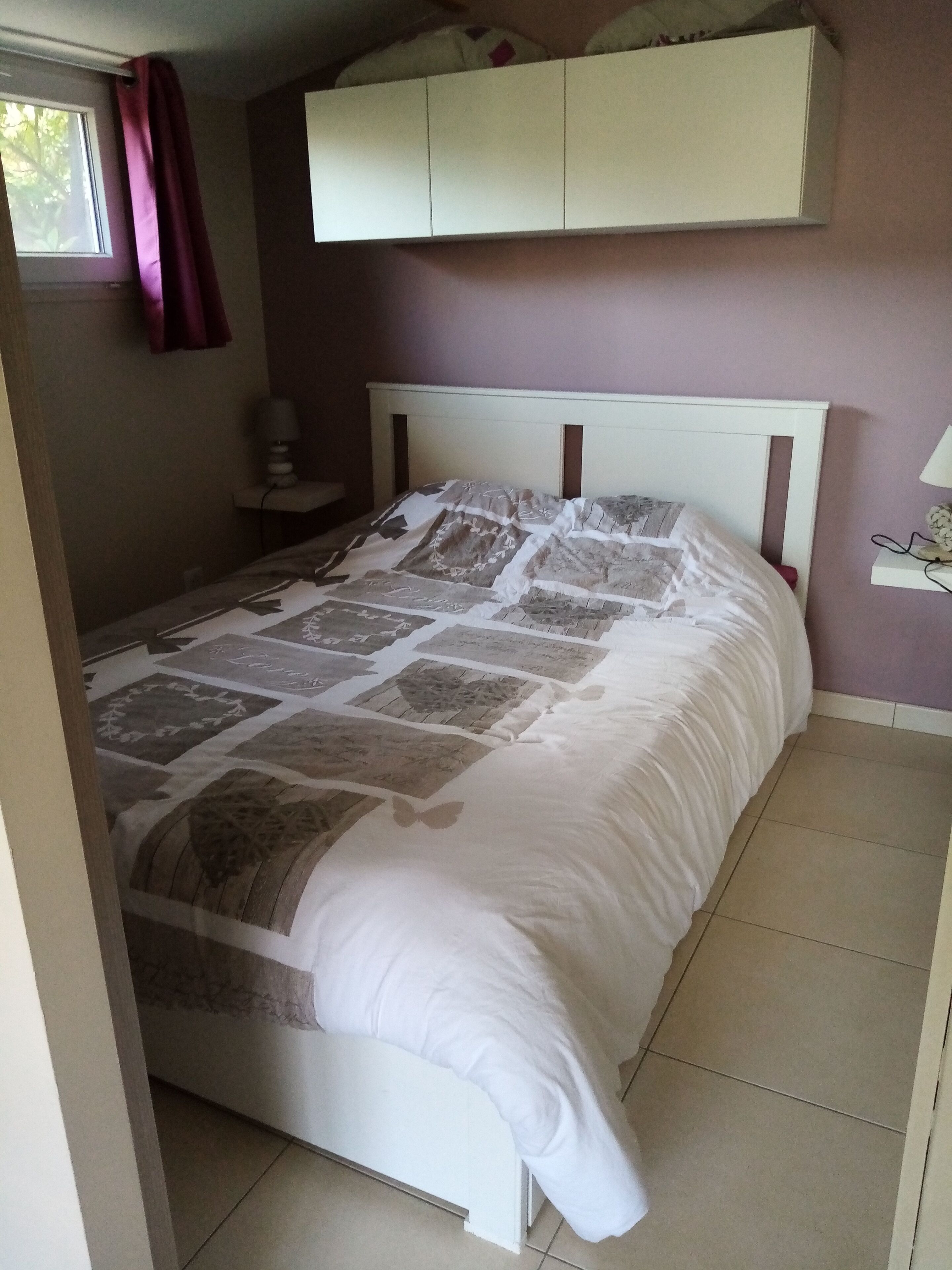 Een slaapkamer met een bed, nachtkastje, lamp en raam met gordijnen.