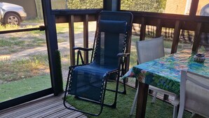 Una terraza techada al aire libre con piso de madera, una mesa con mantel floral y una silla con respaldo de malla.