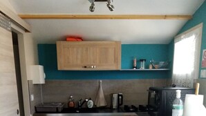 Una cocina compacta con armarios de madera, un microondas, una tetera y una pequeña estantería con utensilios de cocina.