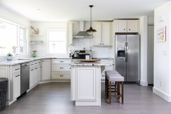 A modern kitchen with white cabinetry, a stainless steel refrigerator, and a central island with stools.