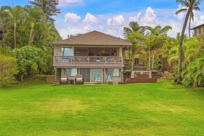 A two-story house with a balcony, surrounded by lush greenery and palm trees.