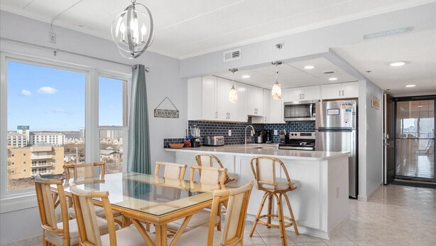 Een moderne keuken met witte kasten, een centraal eiland en een eethoek met rieten stoelen.
