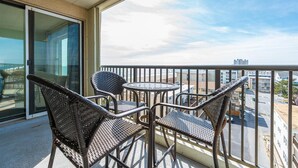 Een balkon met rieten stoelen en een kleine ronde tafel, met uitzicht op een stadslandschap.