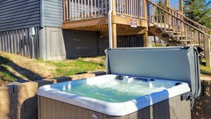 A wooden deck with a hot tub and seating area, a covered porch, and a sign indicating a wildlife-friendly cottage. - The Wildflower Cottage at Mountain Paradise (French Creek)