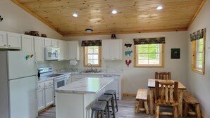 A modern kitchen with white cabinets, a marble countertop, and a wooden ceiling. - The Wildflower Cottage at Mountain Paradise (French Creek)