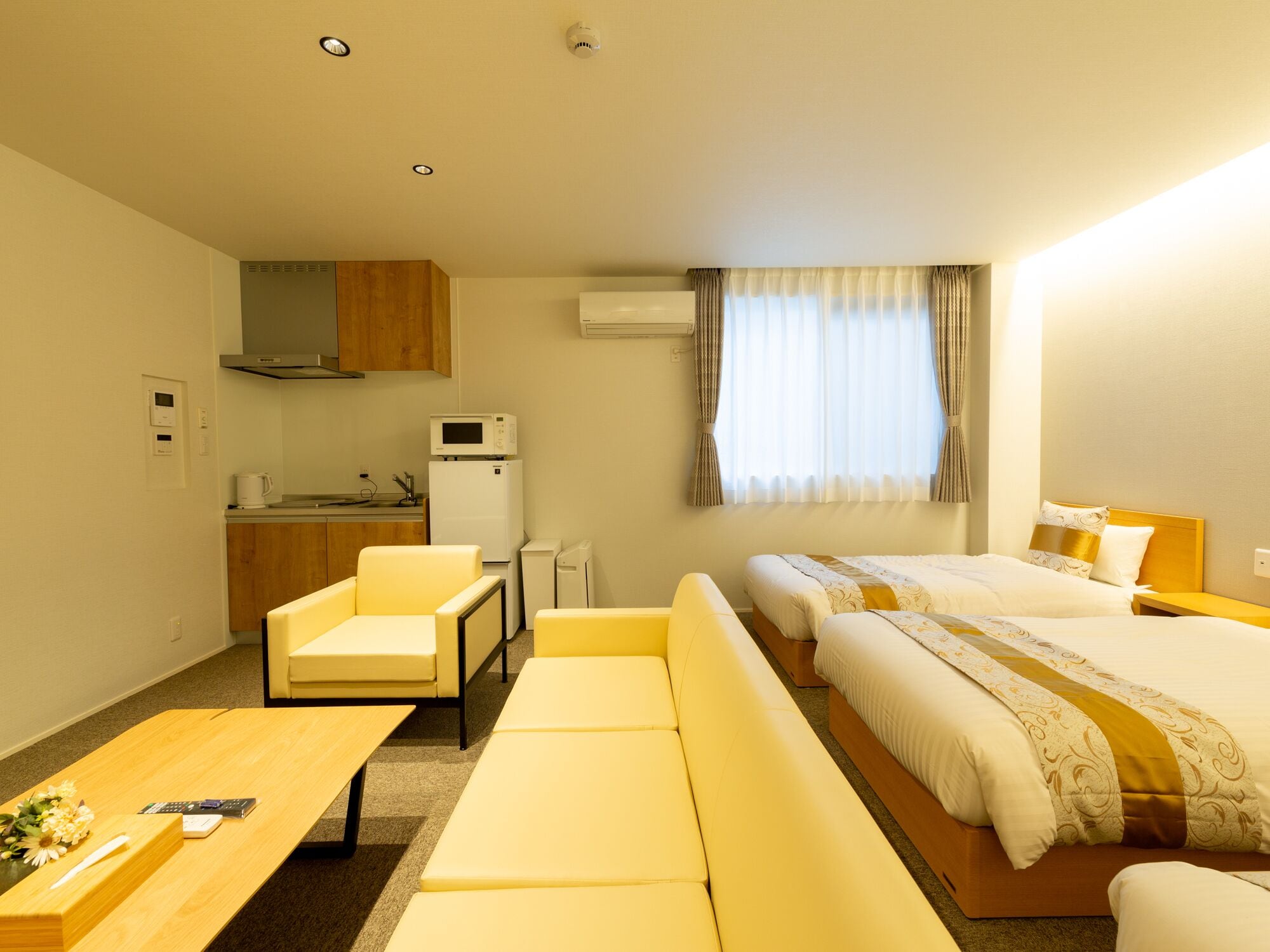 A compact hotel room with a kitchenette, a sofa, a bed, and a small table.