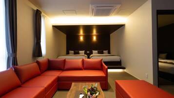 A modern hotel room with a sectional sofa, a wooden coffee table with a vase, and a separate bed area with a headboard.