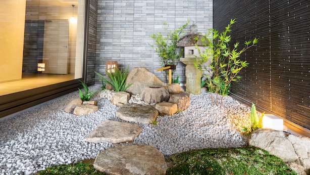Un jardín exterior moderno con un sendero de piedra, rocas y plantas de bambú.