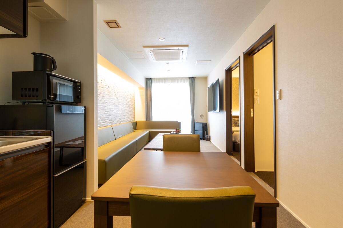 Hotellihuone, jossa on pieni keittiö, ruokailutila, sohva ja televisio.