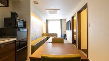 Una habitación de hotel con kitchenette, zona de comedor, sofá y televisor.
