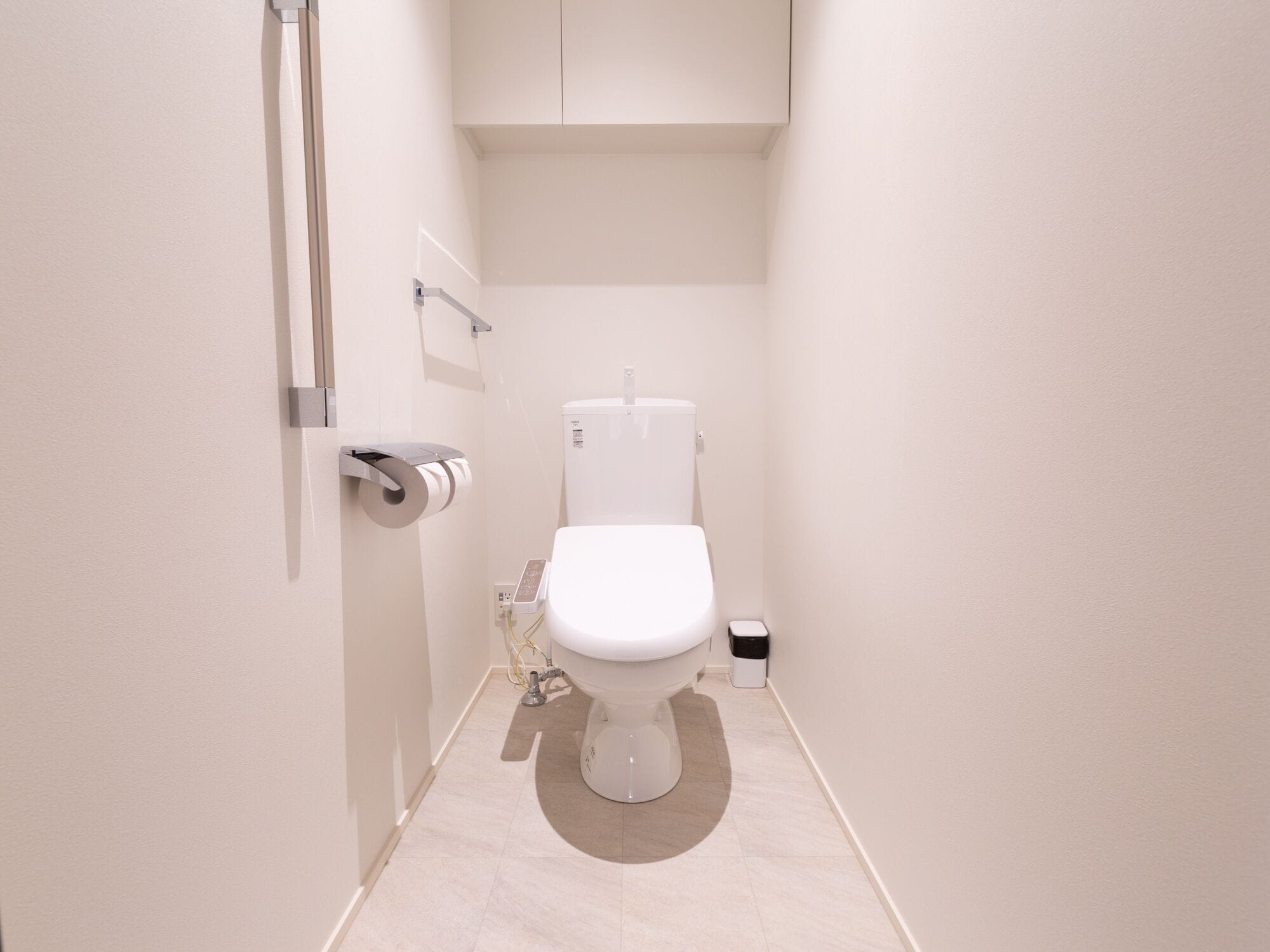 A compact, modern bathroom with a toilet, a toilet paper holder, and a trash bin.