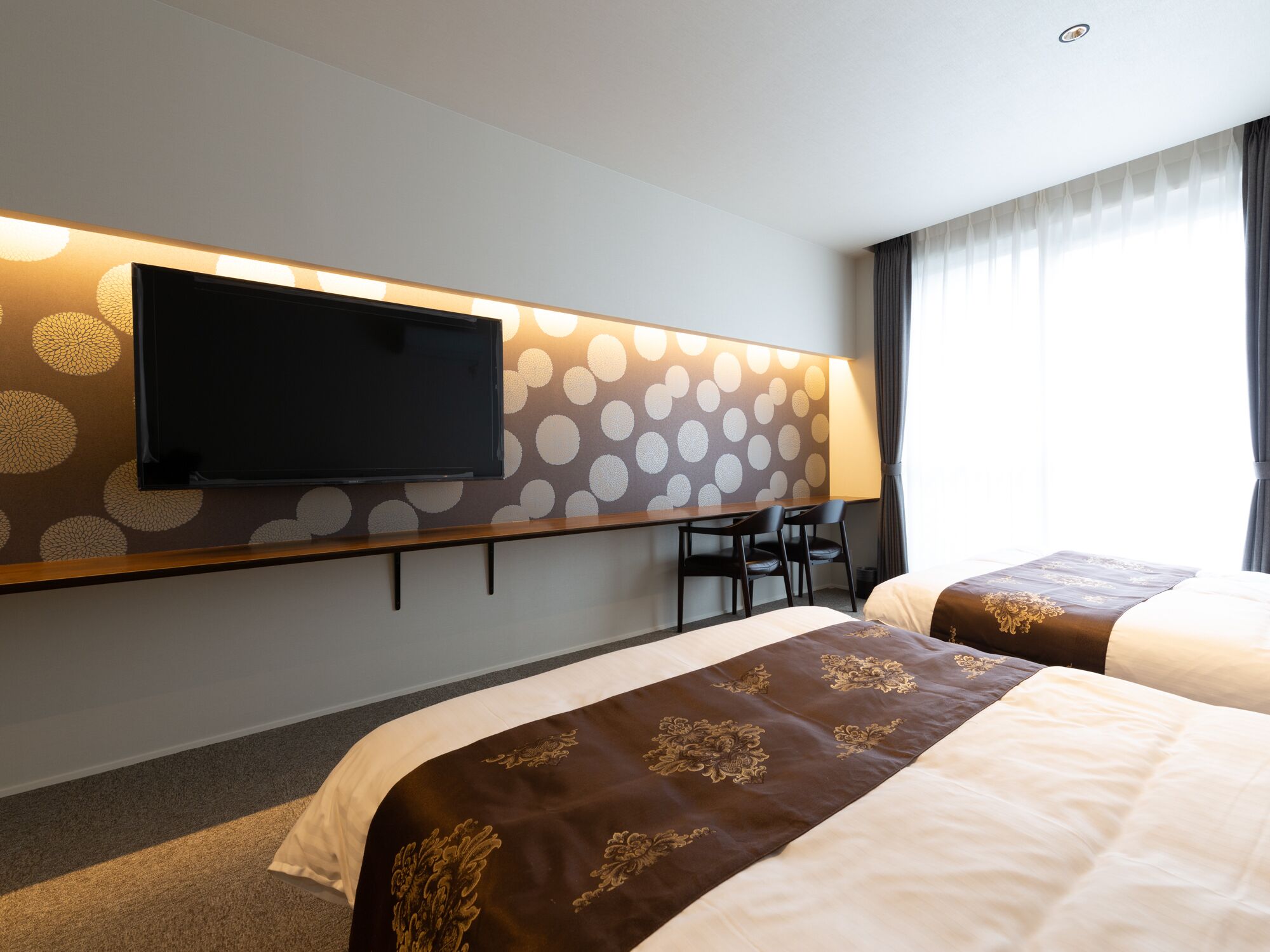 Une chambre d’hôtel avec deux lits, un téléviseur fixé au mur et un coin salon avec des fauteuils.