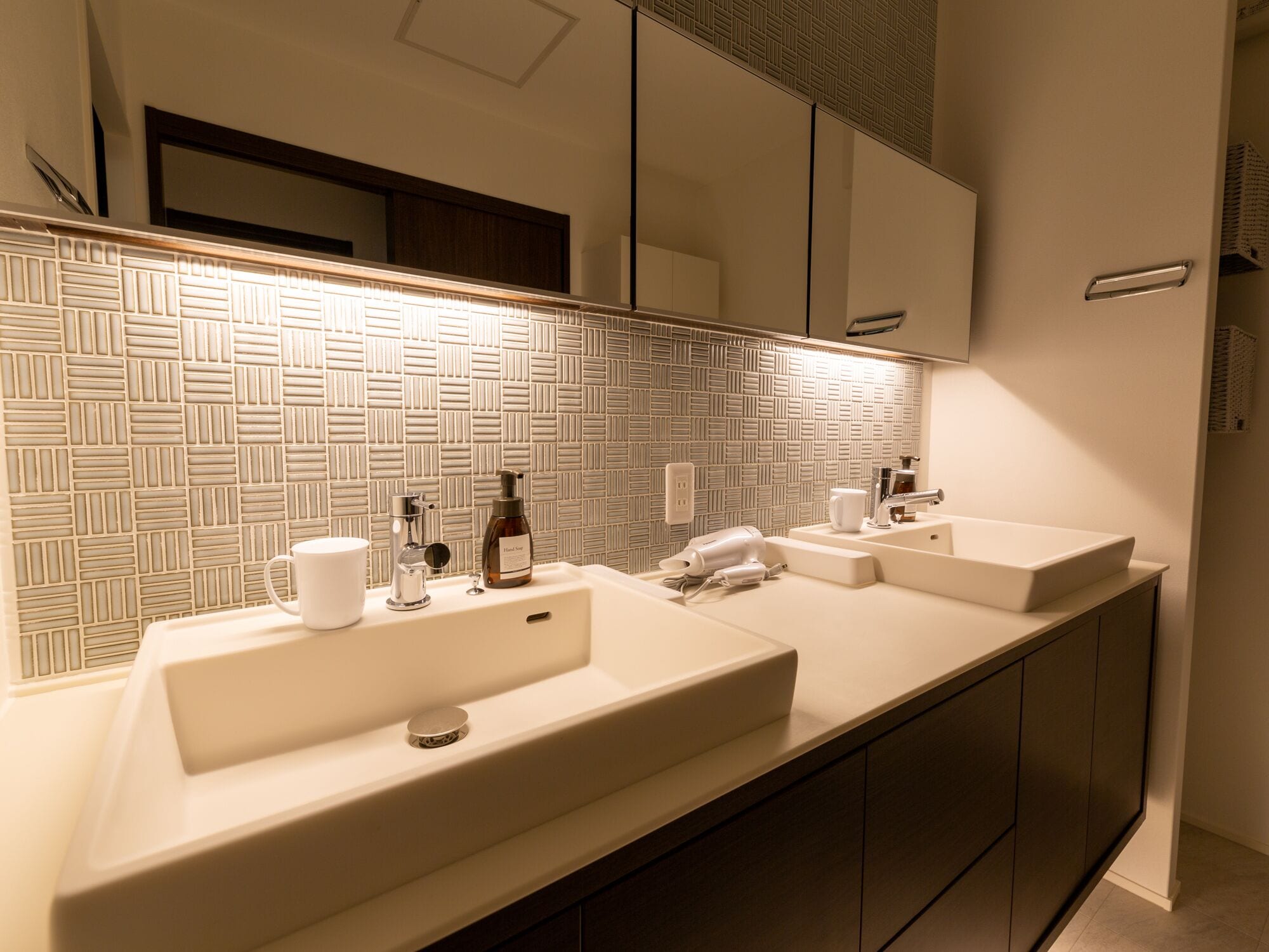 A modern bathroom with a large mirror, two sinks, and a patterned tile backsplash.