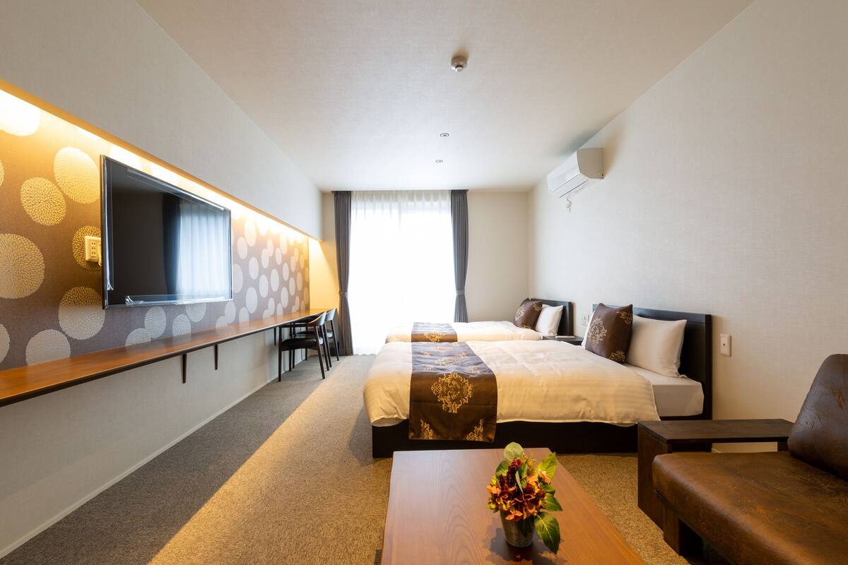 Hotellihuone, jossa on sänky, työpöytä, tuoli, sohva ja televisio.