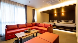 Una habitación de hotel moderna con un sofá rojo, una mesa de centro de madera, un cubo de basura pequeño y una cama con cabecera oscura.