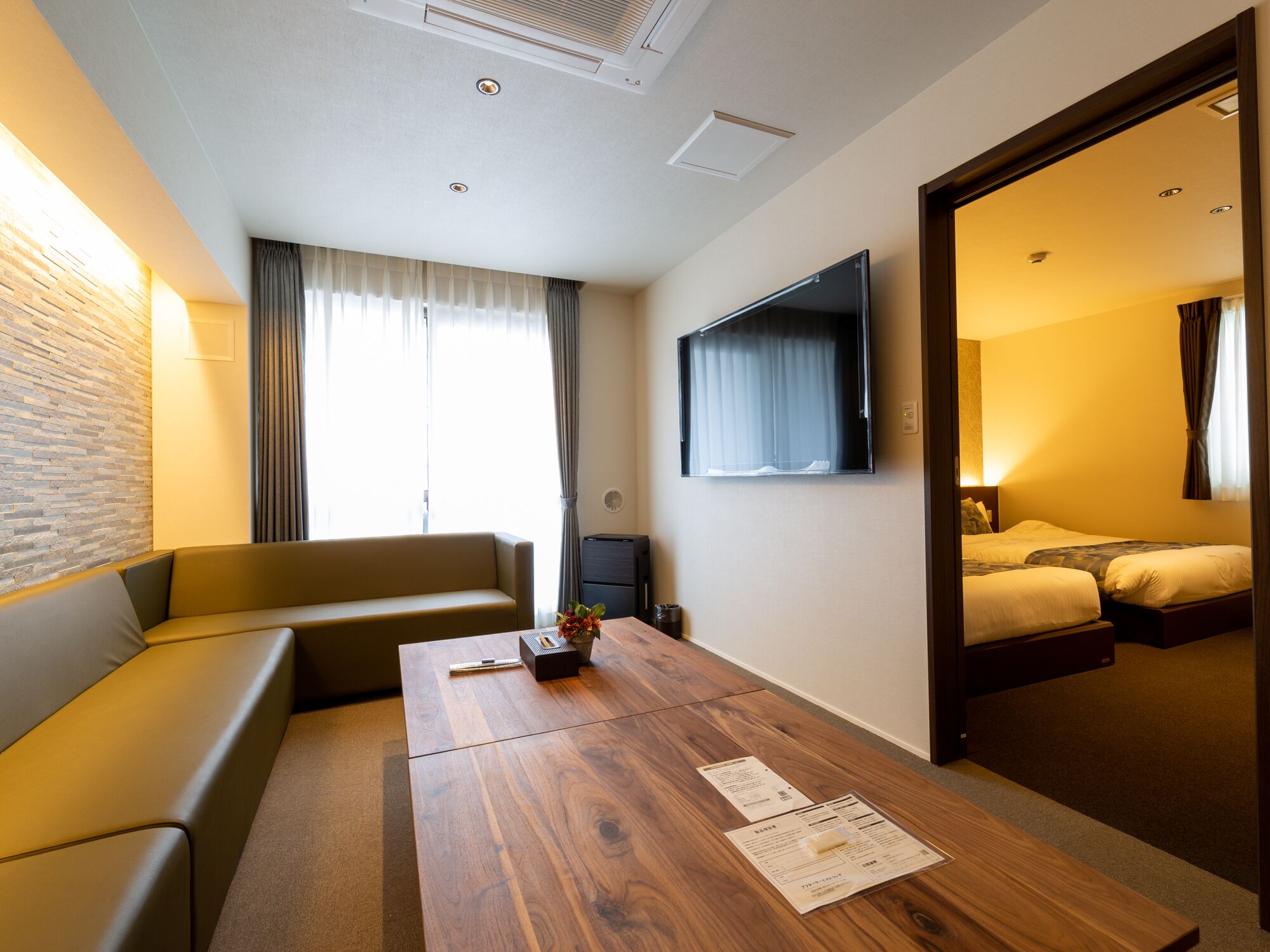 A hotel room with a sofa, a wooden table with papers, a TV, and a bed.