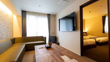 A hotel room with a sofa, a wooden table with papers, a TV, and a bed.