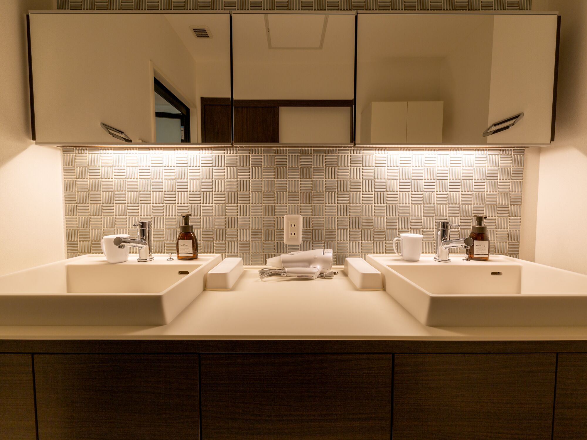 A modern bathroom with two sinks, a mirror, and a patterned backsplash.